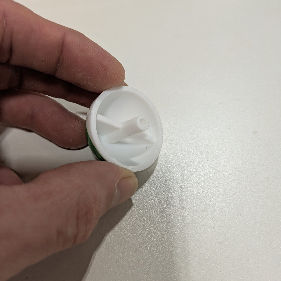 Hand holding a white plastic component against a plain background