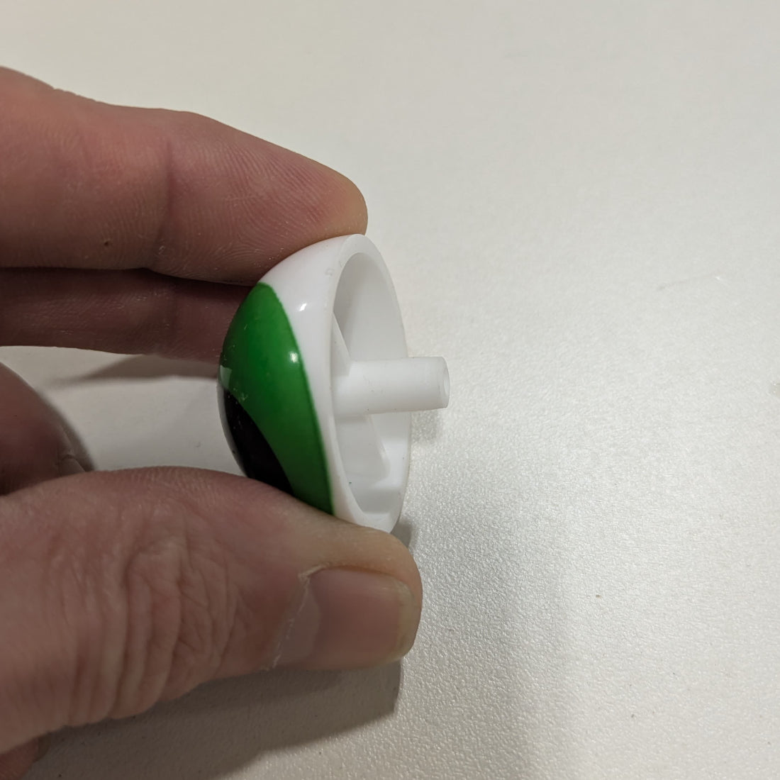 Hand holding a small green and white object against a plain background
