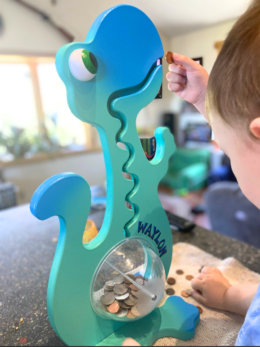 Child playing with a blue and green toy resembling a dinosaur with a coin slot.